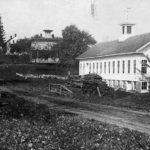 The Village of Hanks Hill. The mill on the right replaced the one that burned in December 1882. The small building across the street is the original 1810 Hanks mill, the first water-powered silk mill in this country. It was purchased by Henry Ford in the 1930s and relocated to Dearborn, Michigan. Continuing up the road is the mill owner’s home and the boarding house for mill workers.